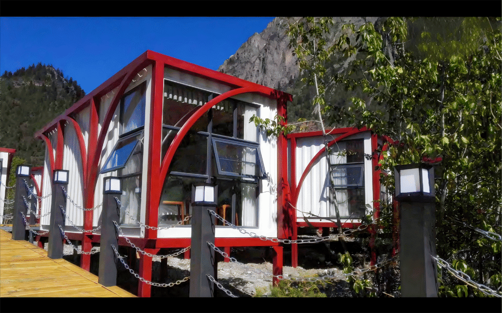 Modern prefab modular tiny home with innovative red and white design, eco-friendly construction, ideal for sustainable living, set against scenic mountainous background.